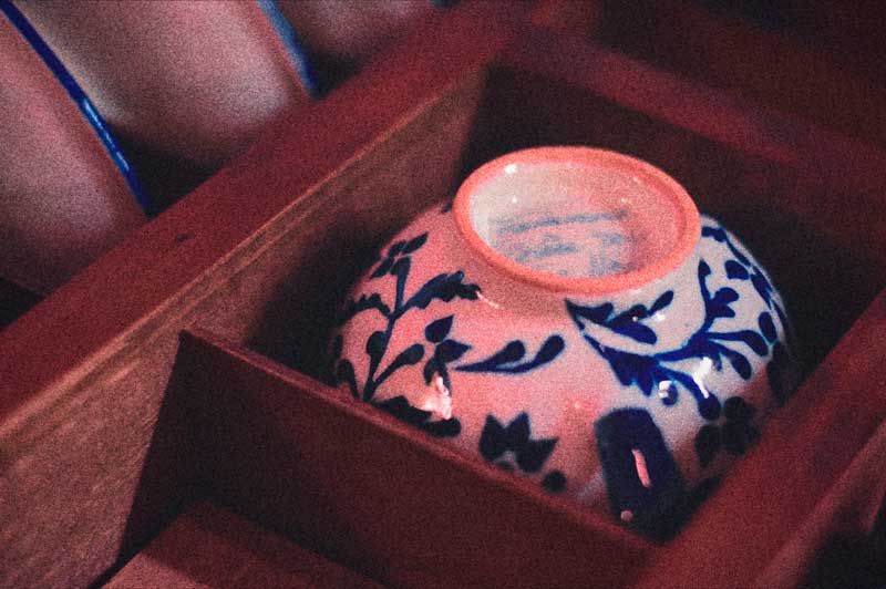 Cuenco de Talavera con flores azules sobre fondo blanco, colocado boca abajo en estante de madera